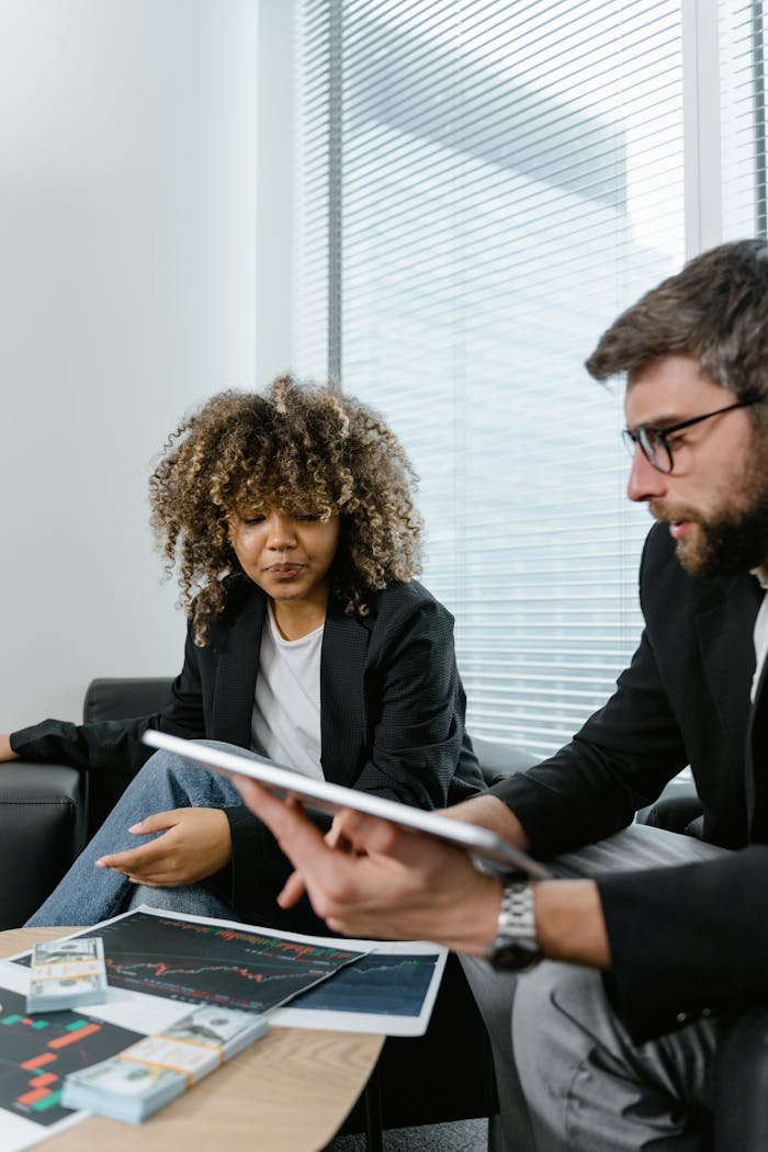 Two professionals discussing financial graphs on a tablet in a modern office setting.